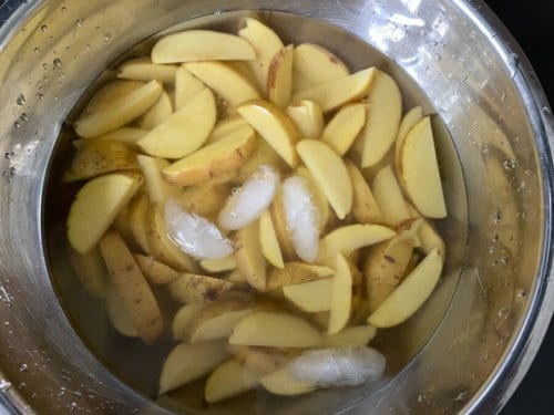 Potato wedges soaked in iced water in a steel bowl