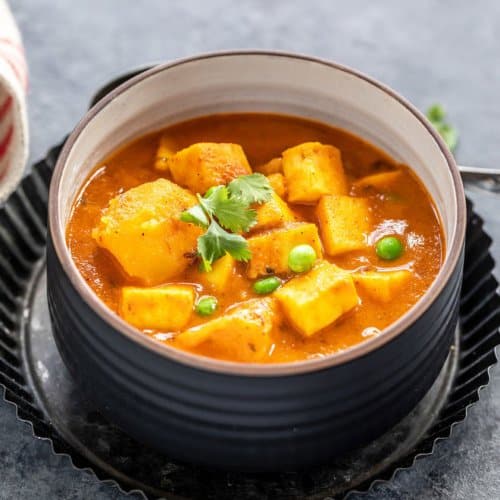 Aloo matar paneer served in a black bowl with white interior