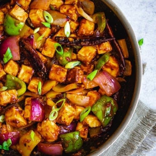 Chili paneer served in a pan garnished with red chillies and chopped green onions