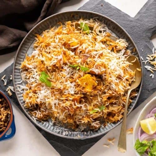 Paneer makhani biryani served in a black plate along with red onions and mint