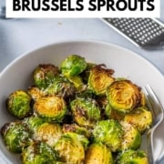 Brussels sprouts served in a white bowl with grated cheese with a fork