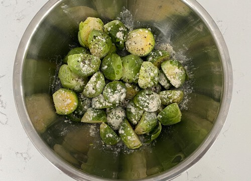 Chopped Brussels sprouts sprinkled with garlic powder and pepper in a steel bowl