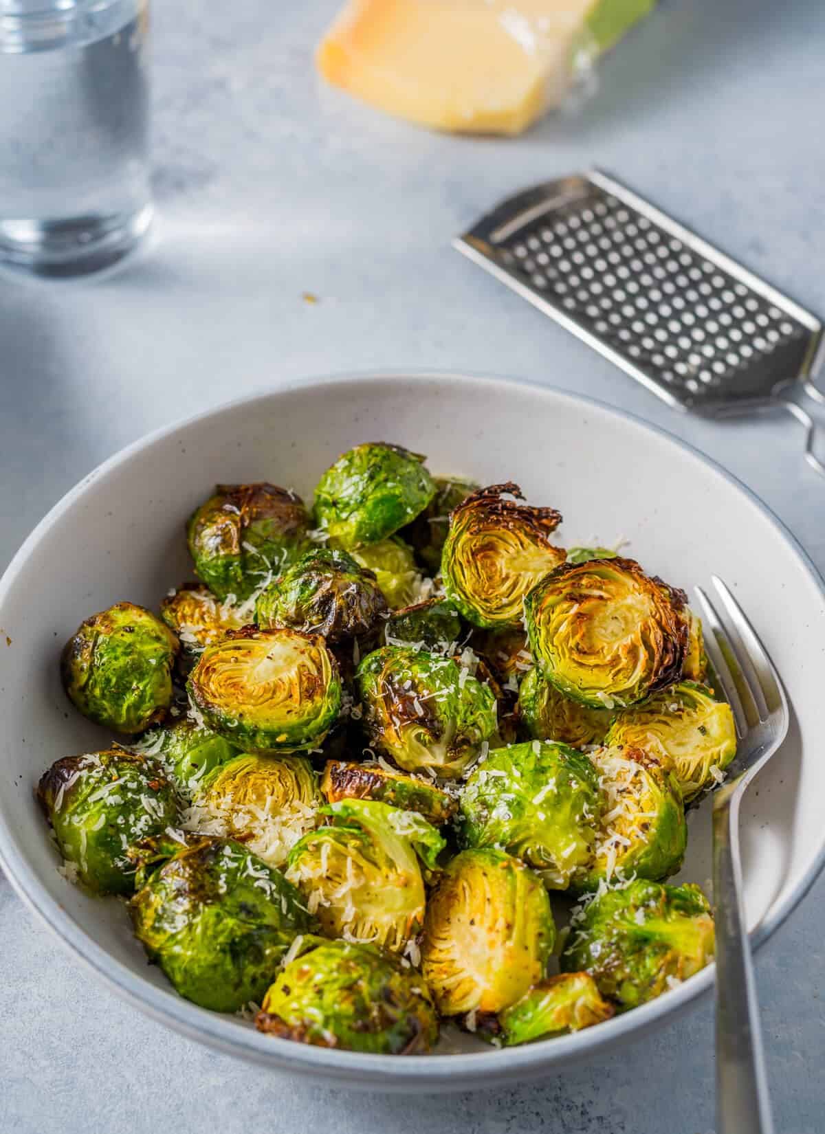Crispy Air Fryer Brussels Sprouts garnished with freshly grated parmesan cheese in a white bowl with a metal fork