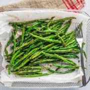Air Fryer Green Beans (Asian-Style) in an air fryer basket lined with parchment paper with a fork