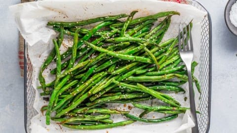 Air Fryer Green Beans (Asian-Style) in an air fryer basket lined with parchment paper with a fork