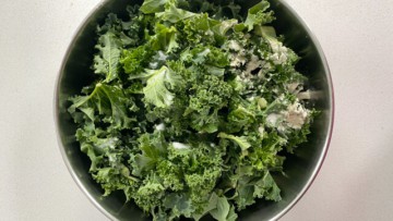 Kale pieces in a steel bowl with seasonings on top