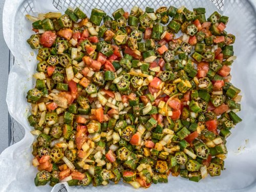 Chopped okra and tomatoes on a parchment lined air fryer rack.