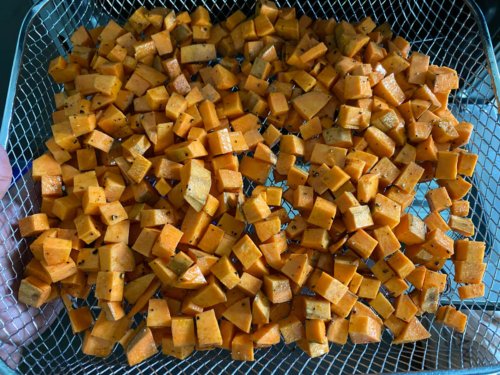 Adding sweet potato cubes to the air fryer tray, being sure not to overcrowd.