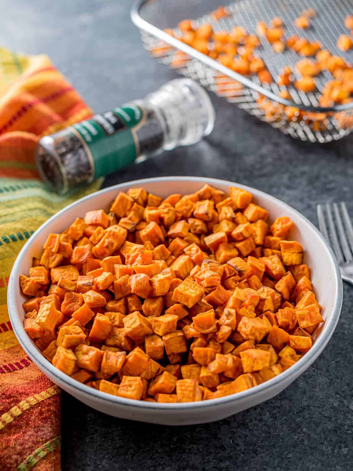 A bowl of air fryer sweet potato cubes, with seasoning in the background.