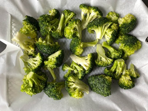 Adding raw broccoli florets to a parchment lined air fryer try.
