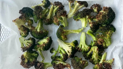 A parchment lined air fryer try with roasted, browned broccoli.