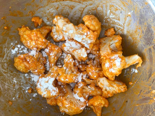 Sprinkling corn starch over cauliflower florets that have been tossed with buffalo sauce.