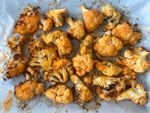 A tray full of cauliflower florets that have been coated in buffalo seasoning and butter, and then air fried until crisp.
