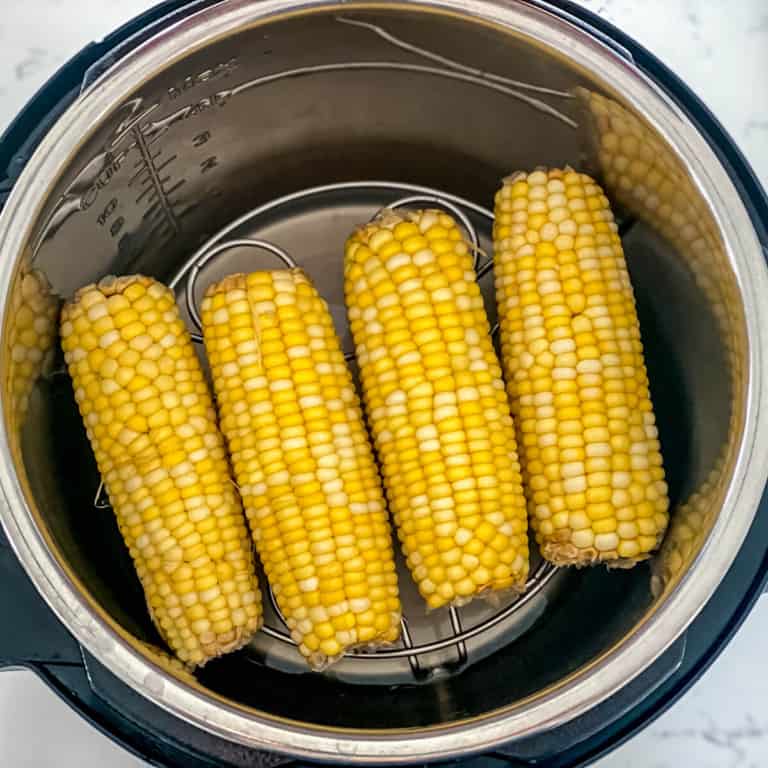 Four cobs of corn lay on top of a trivet inside of an Instant Pot