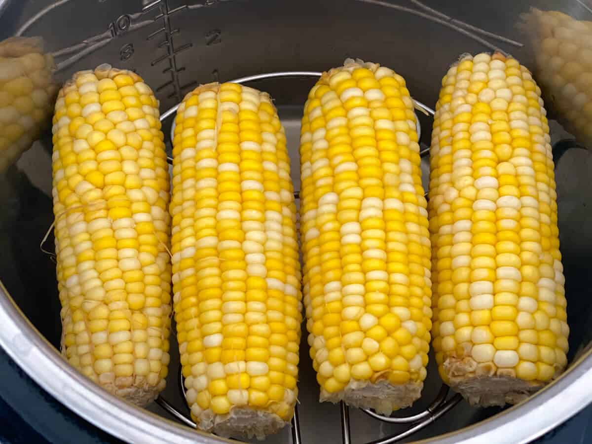 Four cobs of corn, laying on a trivet inside of an Instant Pot.