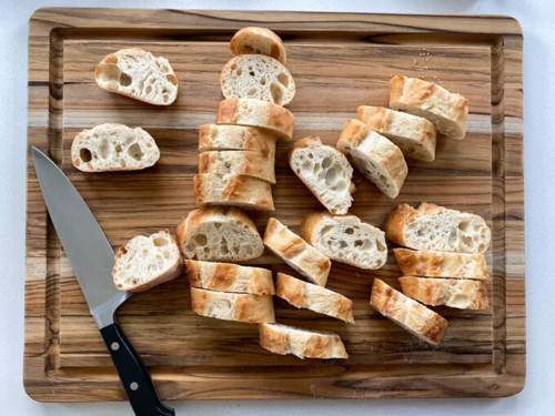 A baguette that has been sliced into 1/2" slices on a cutting board.