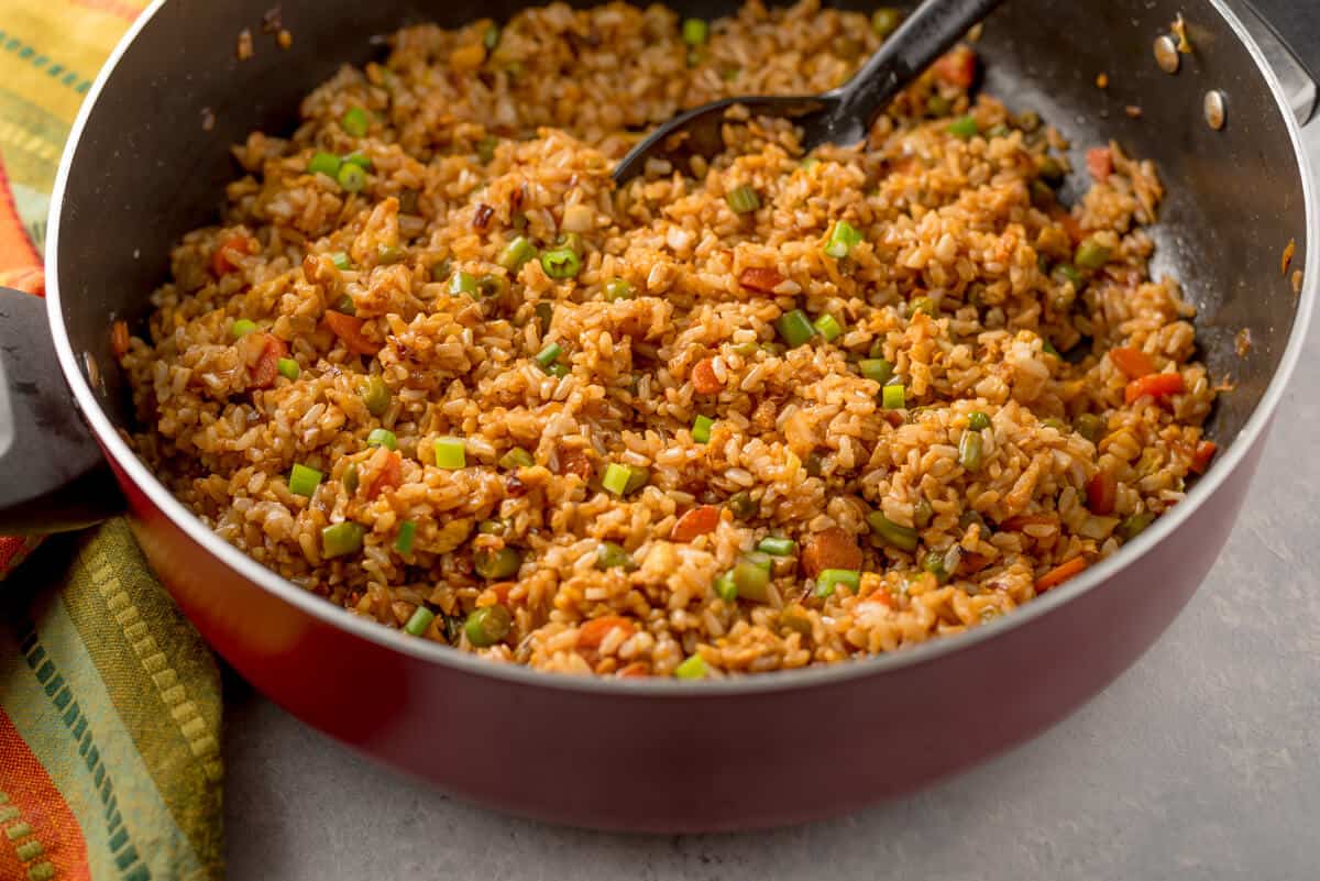 A large red skillet, filled with fried rice, laying on top of a colorful napkin.