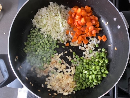 Adding finely chopped vegetables to a skillet, such as carrots and peas.