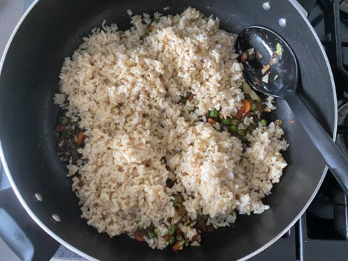 Adding rice to a skillet of vegetables.