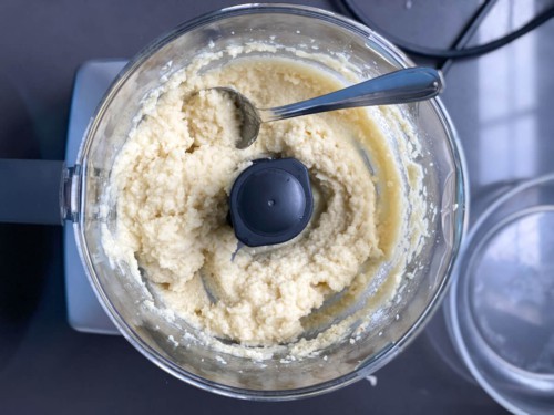 A paste remains in a food processor after blending garlic.