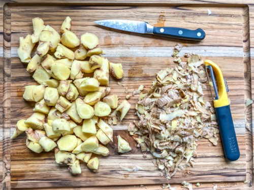 A cutting board with peeled ginger chopped into small pieces.