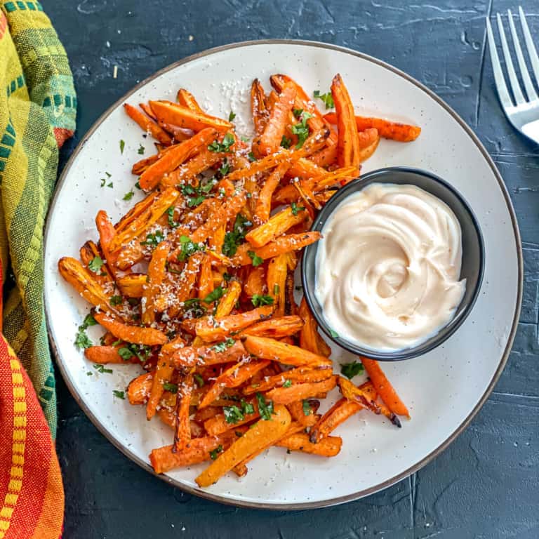 An overheat shot of a plate of roasted carrot fries, with a small bowl of creamy dressing.