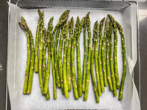 An air fryer basket lined with parchment paper and topped with seasoned asparagus.
