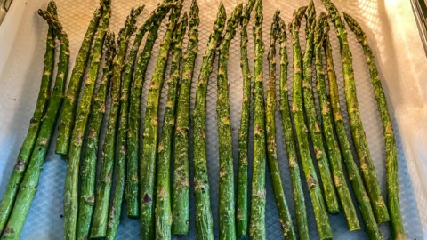 An air fryer basket lined with parchment paper and topped with air fried asparagus.