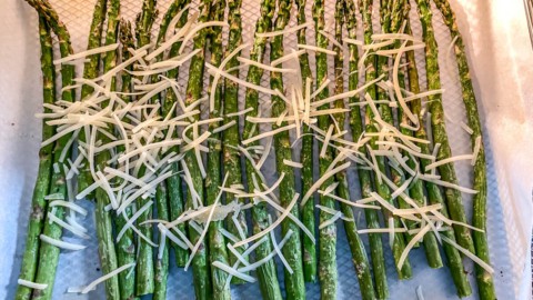 Parmesan topped asparagus on a parchment paper lined air fryer basket before air frying.