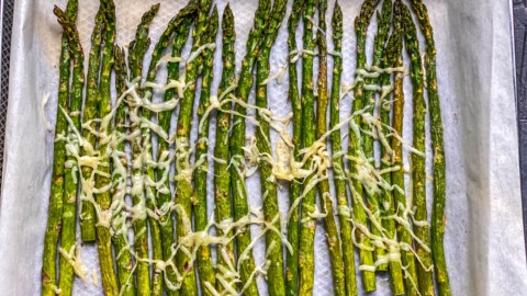 Parmesan topped asparagus on a parchment paper lined air fryer basket after air frying.