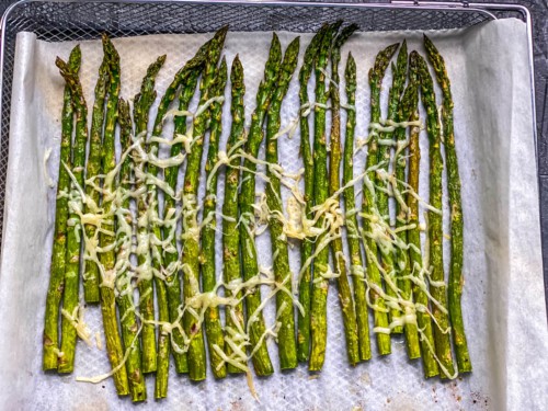 Parmesan topped asparagus on a parchment paper lined air fryer basket after air frying.