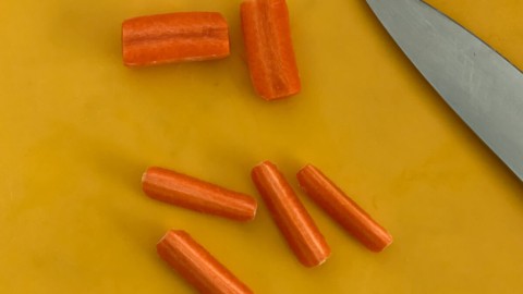 Cutting carrots into quarters on a chopping board.