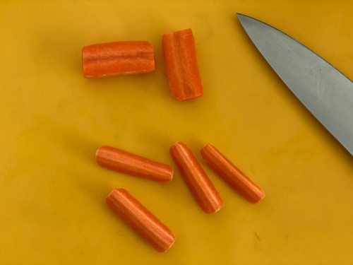 Cutting carrots into quarters on a chopping board.