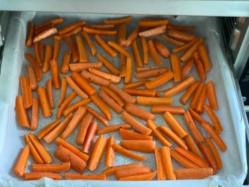 A parchment lined sultry tray with chopped carrots, going into an air fryer.