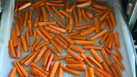 A parchment lined baking tray with chopped carrots, going into an air fryer.