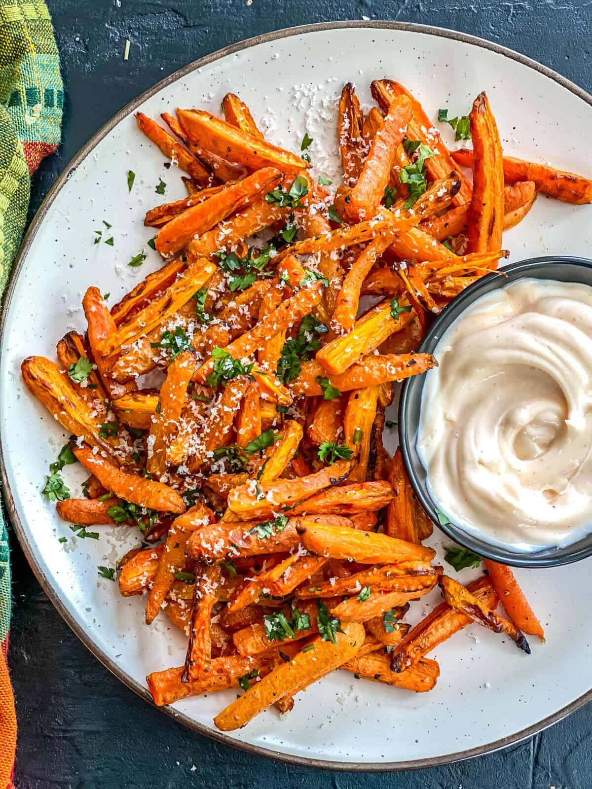 A plate filled with carrot sticks, garnished with parsley and served with a creamy dip on the side.