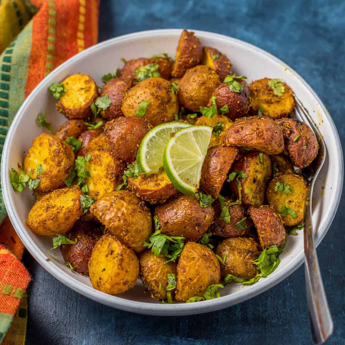A white bowl of baby potatoes, garnished with parsley and lime wedges.