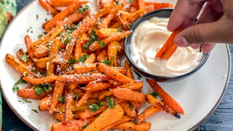 Carrot sticks being dipped into a creamy sauce.