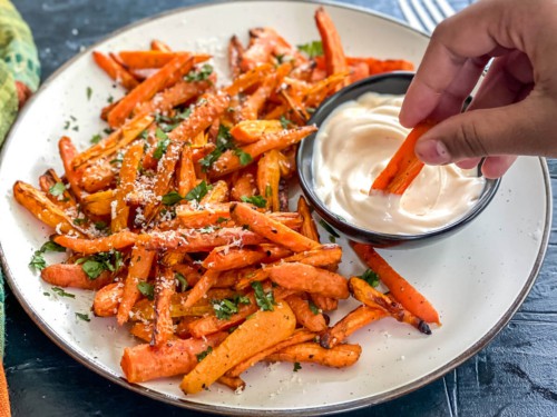 Carrot sticks being dipped into a creamy sauce.
