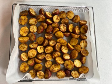 Adding halved victual potatoes to a tray of an air fryer.