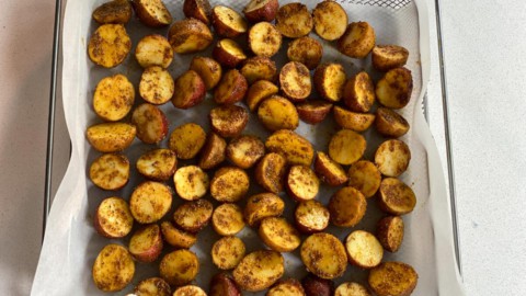 Adding halved baby potatoes to a tray of an air fryer.