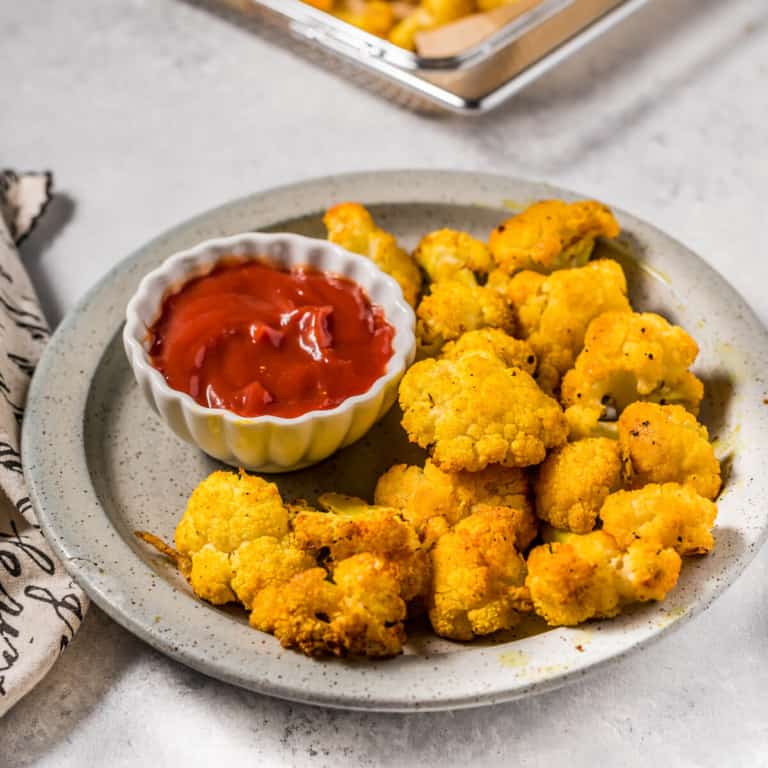 A plate of bright colored cauliflower with a small dish of ketchup on the side.