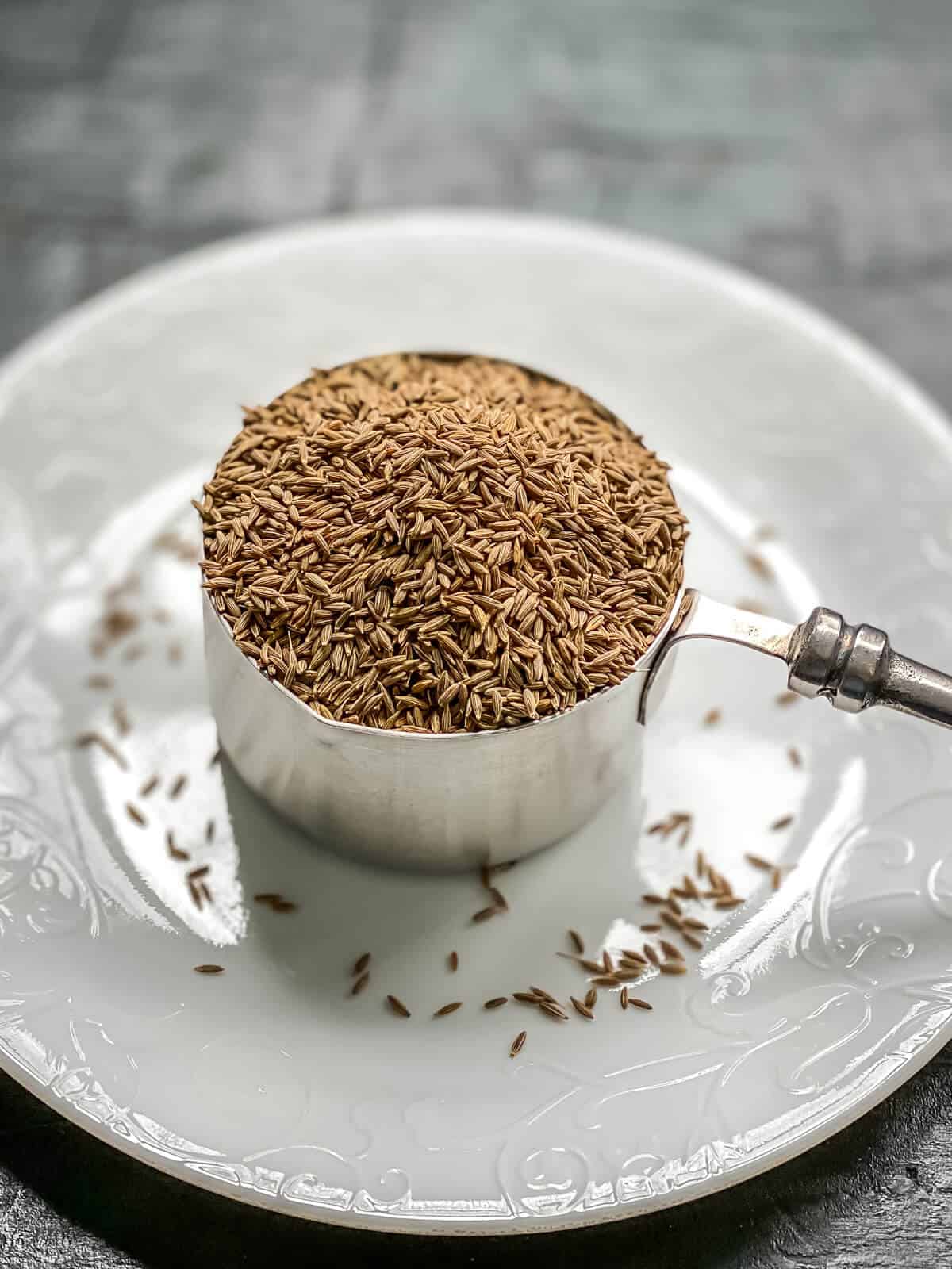 Cumin seeds in a measuring cup placed on a white plate
