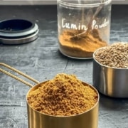 A large measuring cup with cumin powder overflowing.