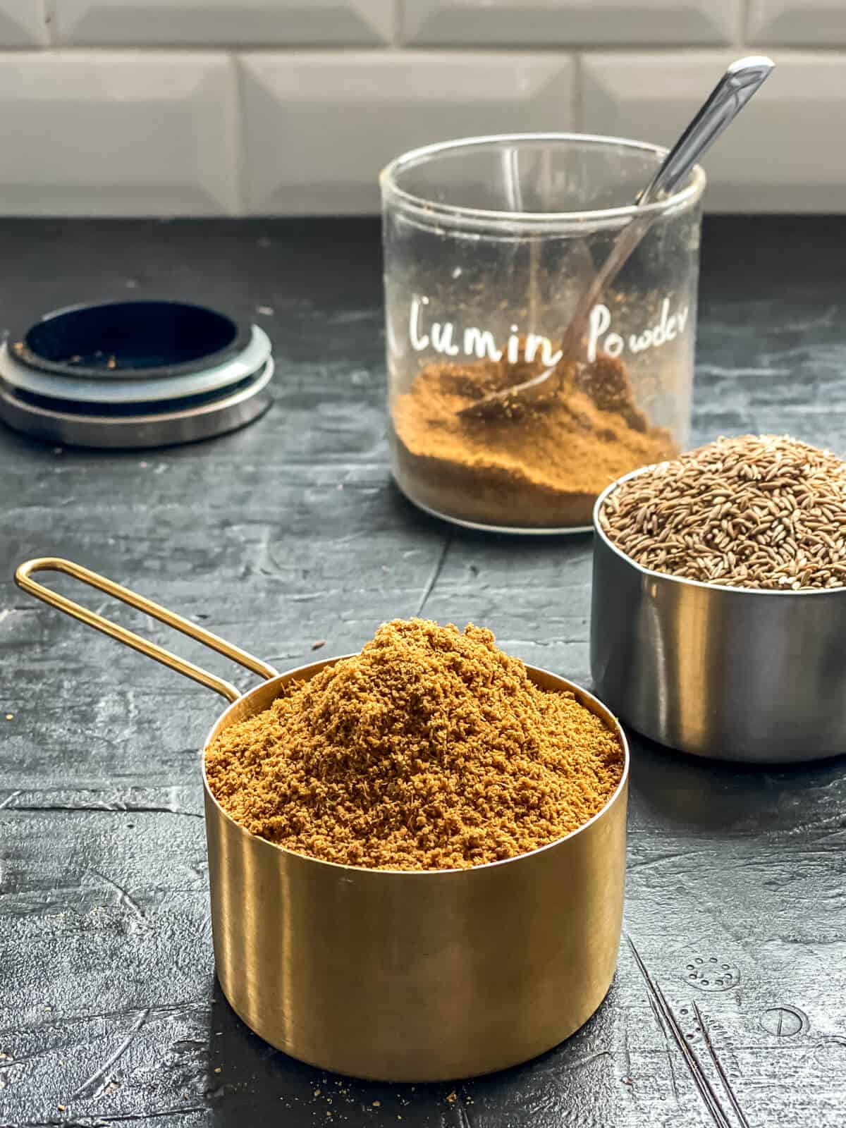 A large scoop of cumin powder, with another scoop of cumin seeds behind it.