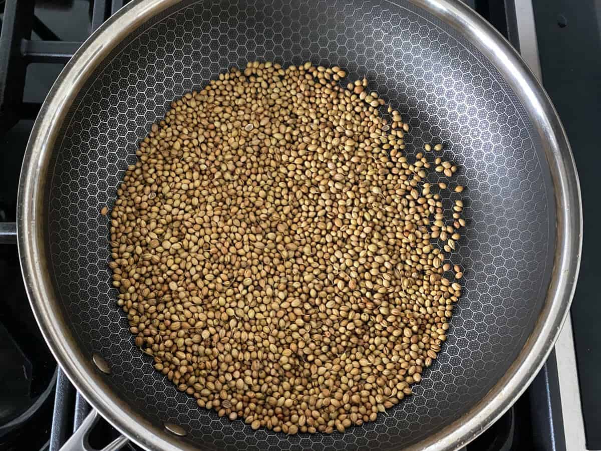 A non-stick skillet with coriander seeds before toasting.