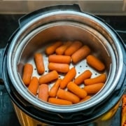 An instant pot with a steamer basket filled with cooked carrots and the words Instant Pot Steamed Carrots at the top.
