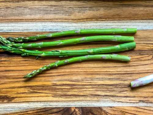 A wooden cutting board with a visual of how to trim the ends off asparagus.