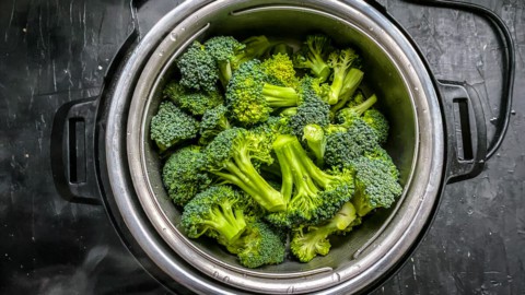 An instant pot with the steamer basket filled with raw broccoli.