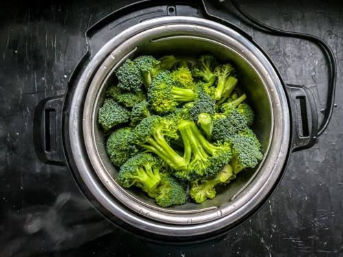 An instant pot with the steamer basket filled with raw broccoli.